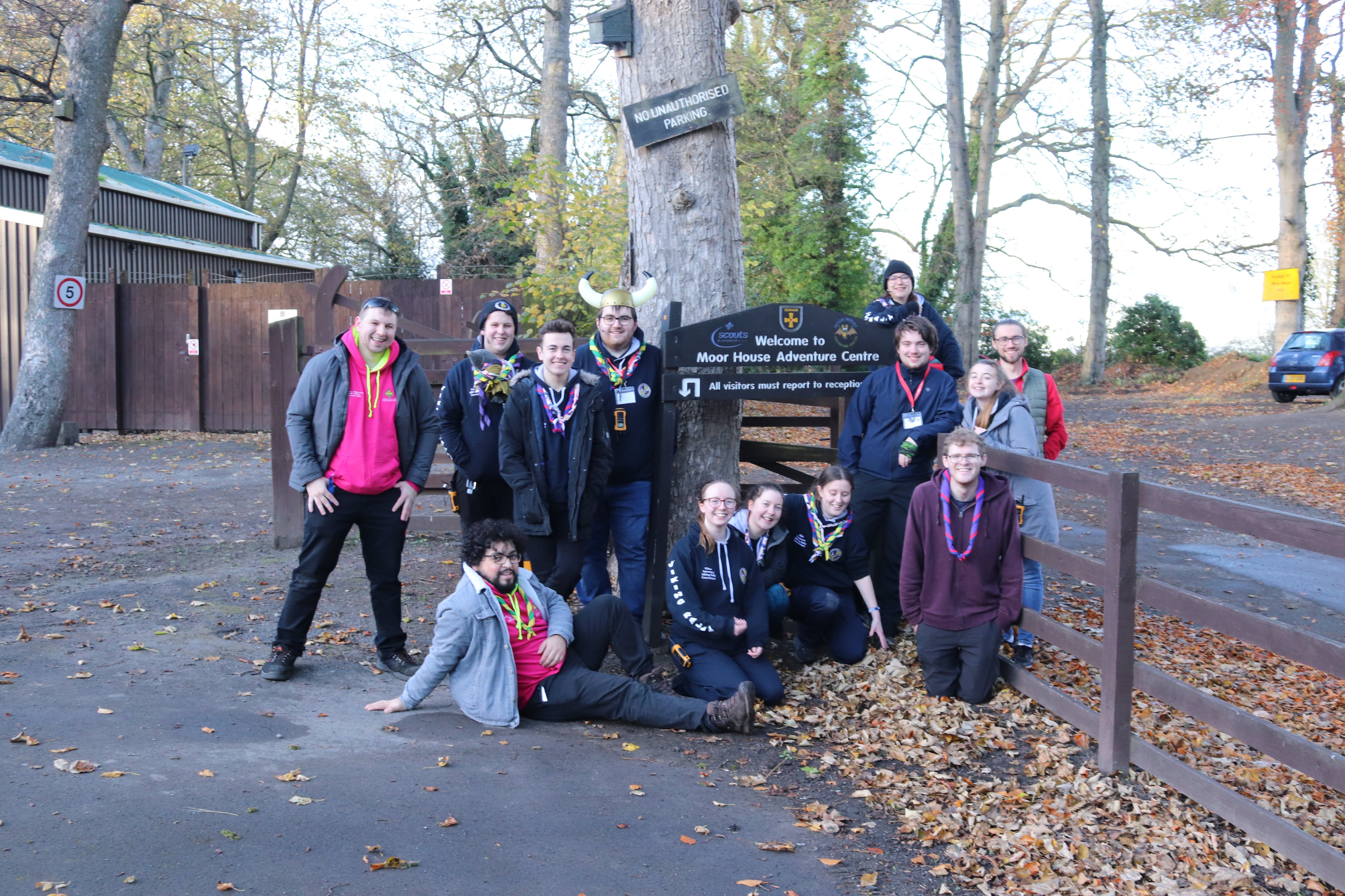 The Viking Rally committee, plus Samir Soares (SSAGO Chair), Ant Gathercole (SSAGO Events Officer) and Jamie Greenwood (NUSSAGG Associate), in front of the campsite sign in the carpark, doing silly poses